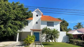 A white building with a red-tiled roof, a small tower, and a blue door.