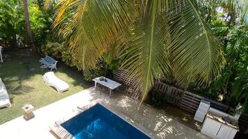 A swimming pool surrounded by palm trees and a wooden deck with lounge chairs.
