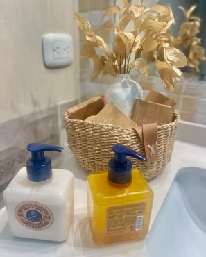 Ein Badezimmer-Waschtisch mit zwei Seifenspendern und einem Korbwägelchen mit verschiedenen Gegenständen.