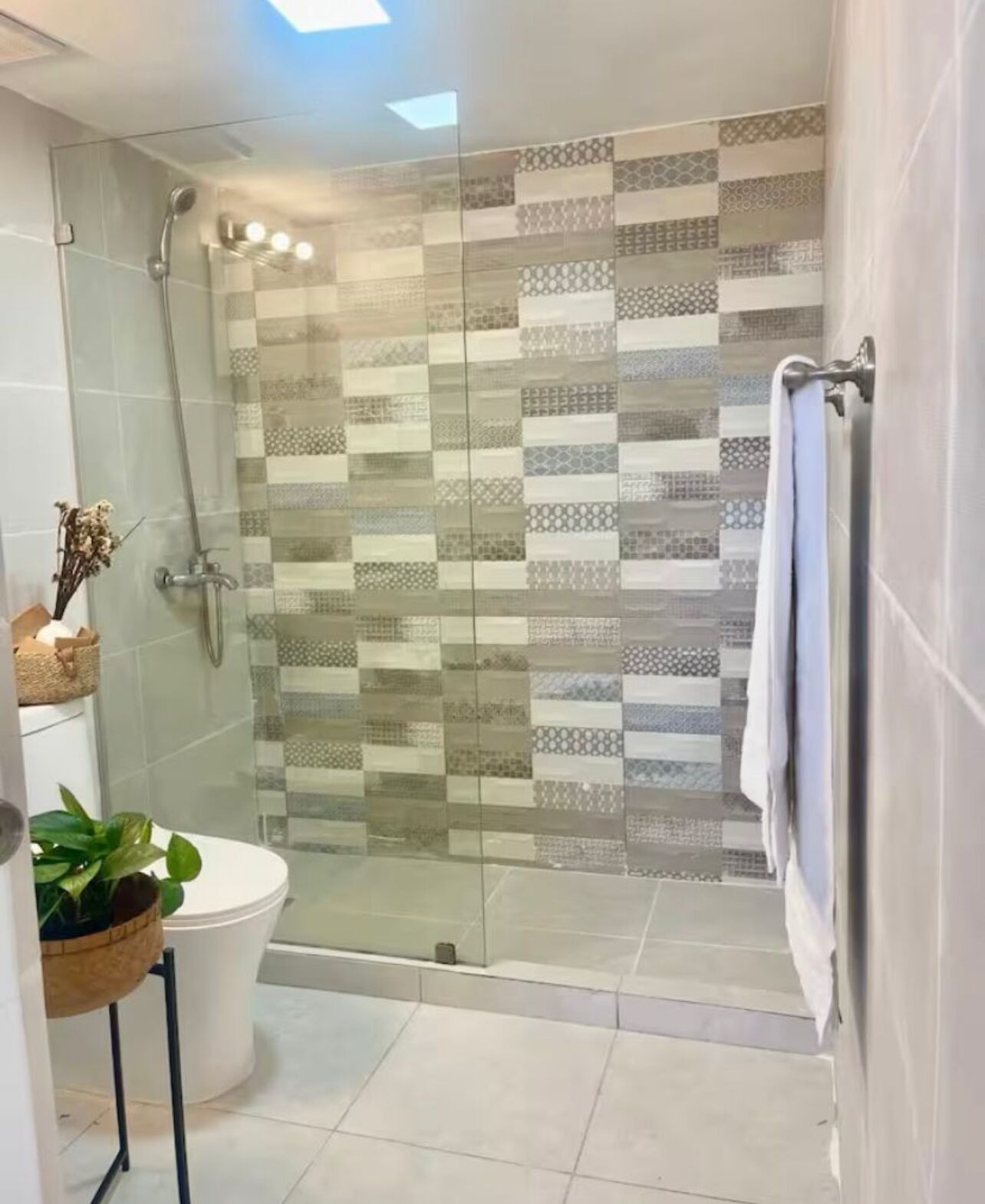 A modern bathroom with a glass shower enclosure, a toilet, and a small sink area.