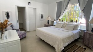 Une chambre à coucher comprenant un lit, des tables de chevet, une commode, une fenêtre avec des rideaux et un luminaire suspendu.