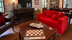 A cozy living room with a wooden ceiling, stone walls, a red sofa, a wooden coffee table, and a chessboard. - Villa Acroria in Karpenisi (Karpenisi)