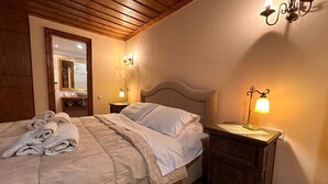 A neatly made bed with a folded towel, a wooden headboard, and two bedside tables with wall-mounted lamps. - Villa Acroria in Karpenisi (Karpenisi)