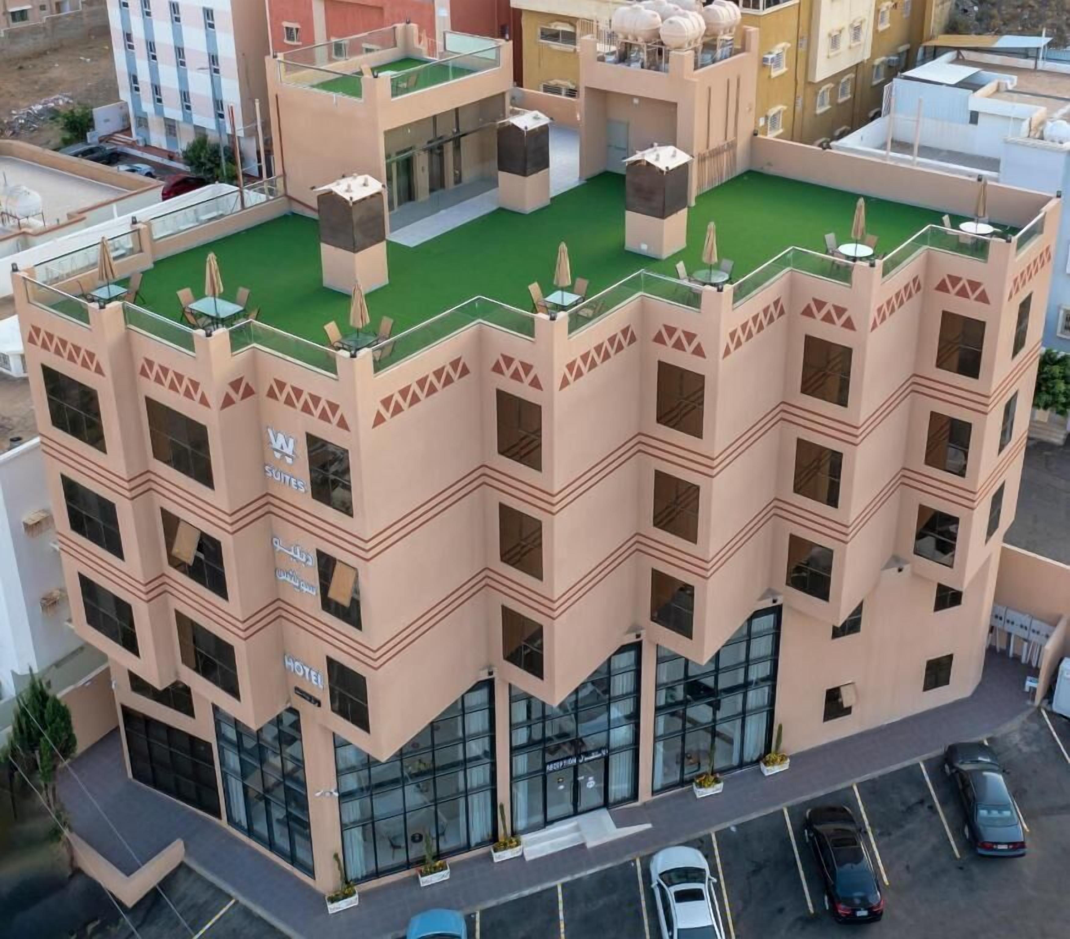 A multi-story hotel with a rooftop terrace, large windows, and a parking area.