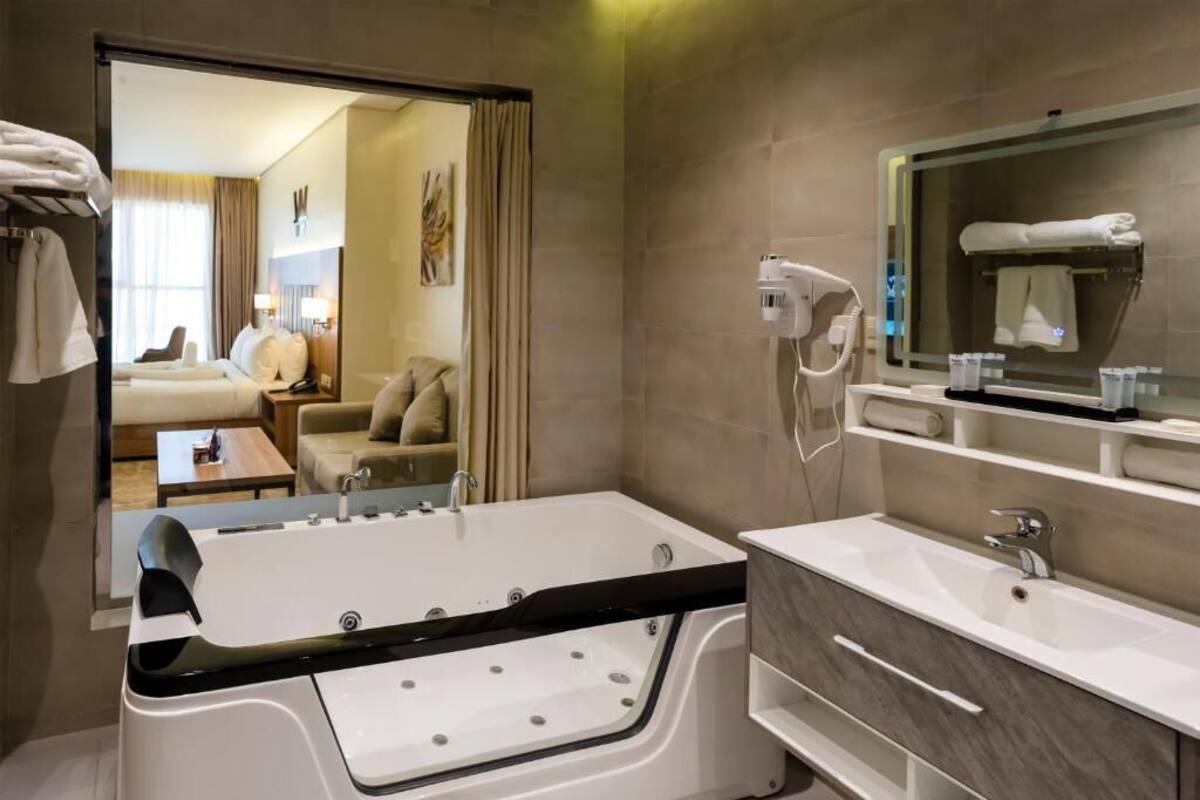 A modern bathroom with a large bathtub, a separate shower area, a vanity with a mirror, and a hairdryer mounted on the wall.