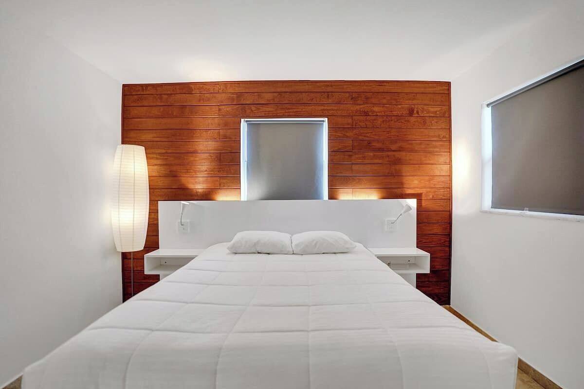 Una habitación de hotel moderna con una pared de acento de madera, una cama grande, una mesita de noche y una ventana.