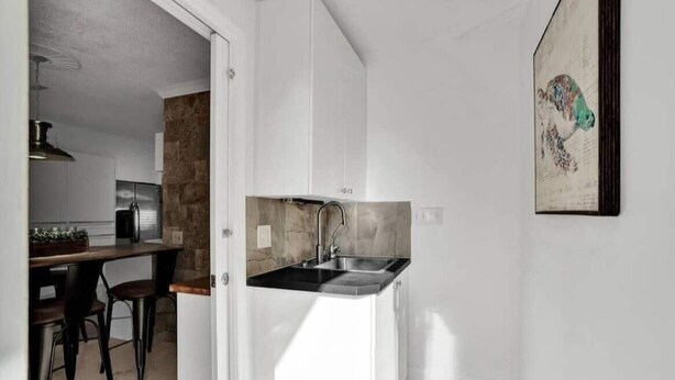 Een compacte keuken met een ingebouwde spoelbak, een eethoek met stoelen en een kunstwerk aan de muur.