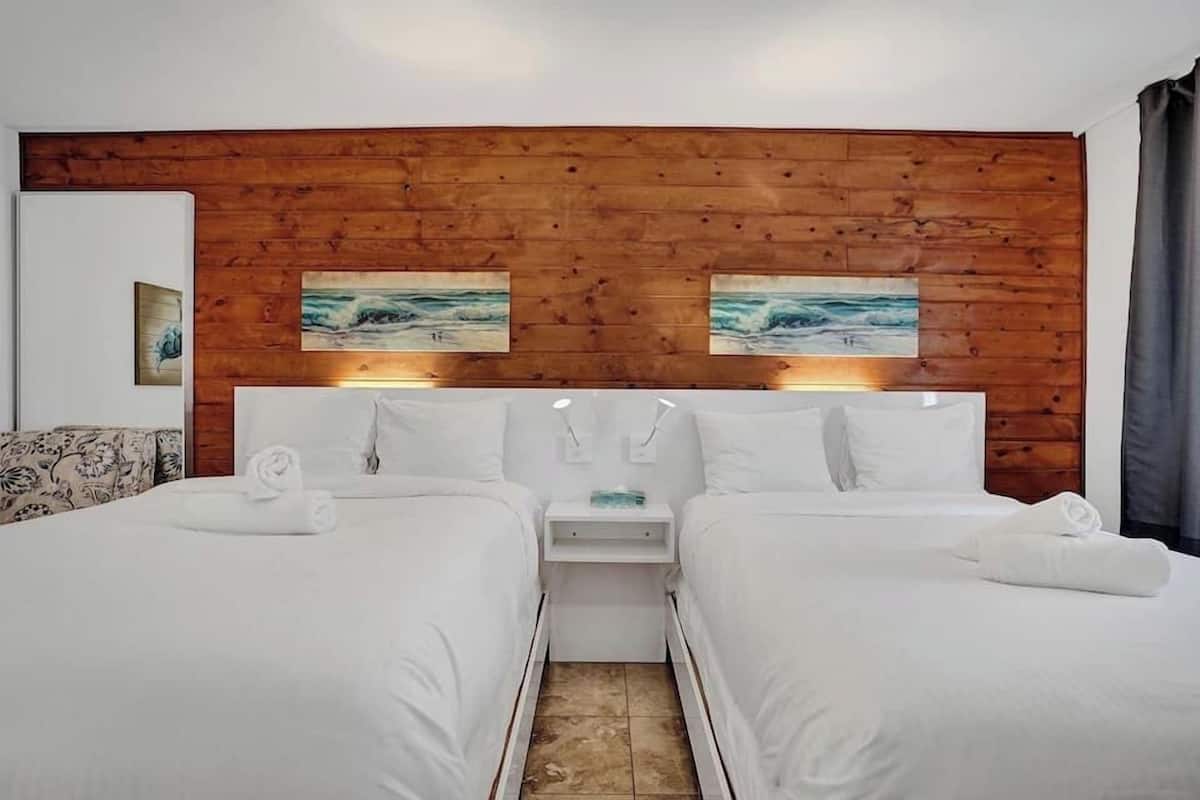Habitación de hotel con dos camas, paneles de madera en la pared y una obra de arte sobre ellas.