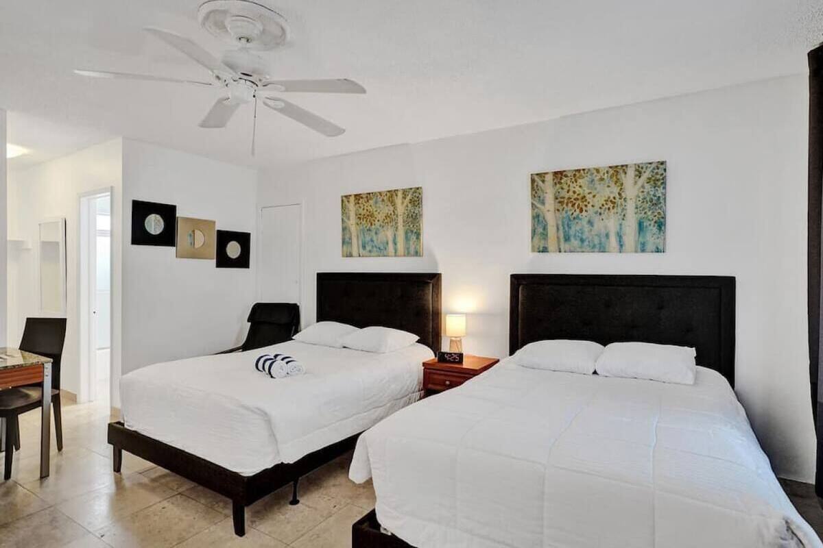 Habitación de hotel con dos camas, ventilador de techo, obras de arte en las paredes y un escritorio con silla.