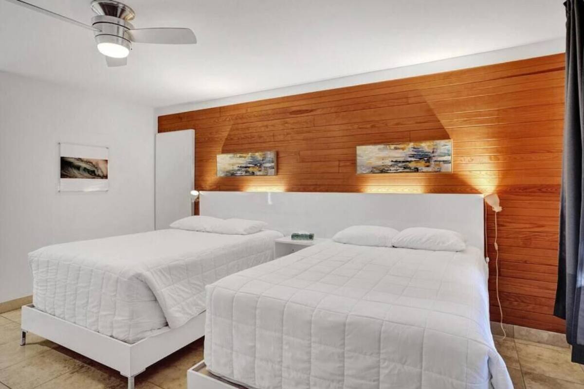 Un dormitorio con dos camas, paneles de madera en la pared y obras de arte sobre ellas.