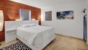 Een moderne slaapkamer met een wit bed, een wand van houten panelen, twee ramen en een schilderij.