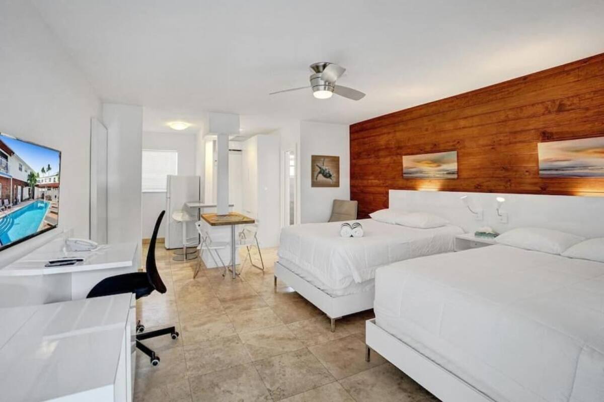Habitación de hotel con dos camas, un escritorio, una silla, ventilador de techo y obra de arte en la pared de madera.