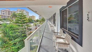 Een balkon met witte stoelen, een houten plafond en uitzicht op palmbomen en gebouwen.