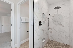 Une salle de bain aux murs recouverts de marbre, une douche avec un pommeau de douche amovible et un porte-serviettes.
