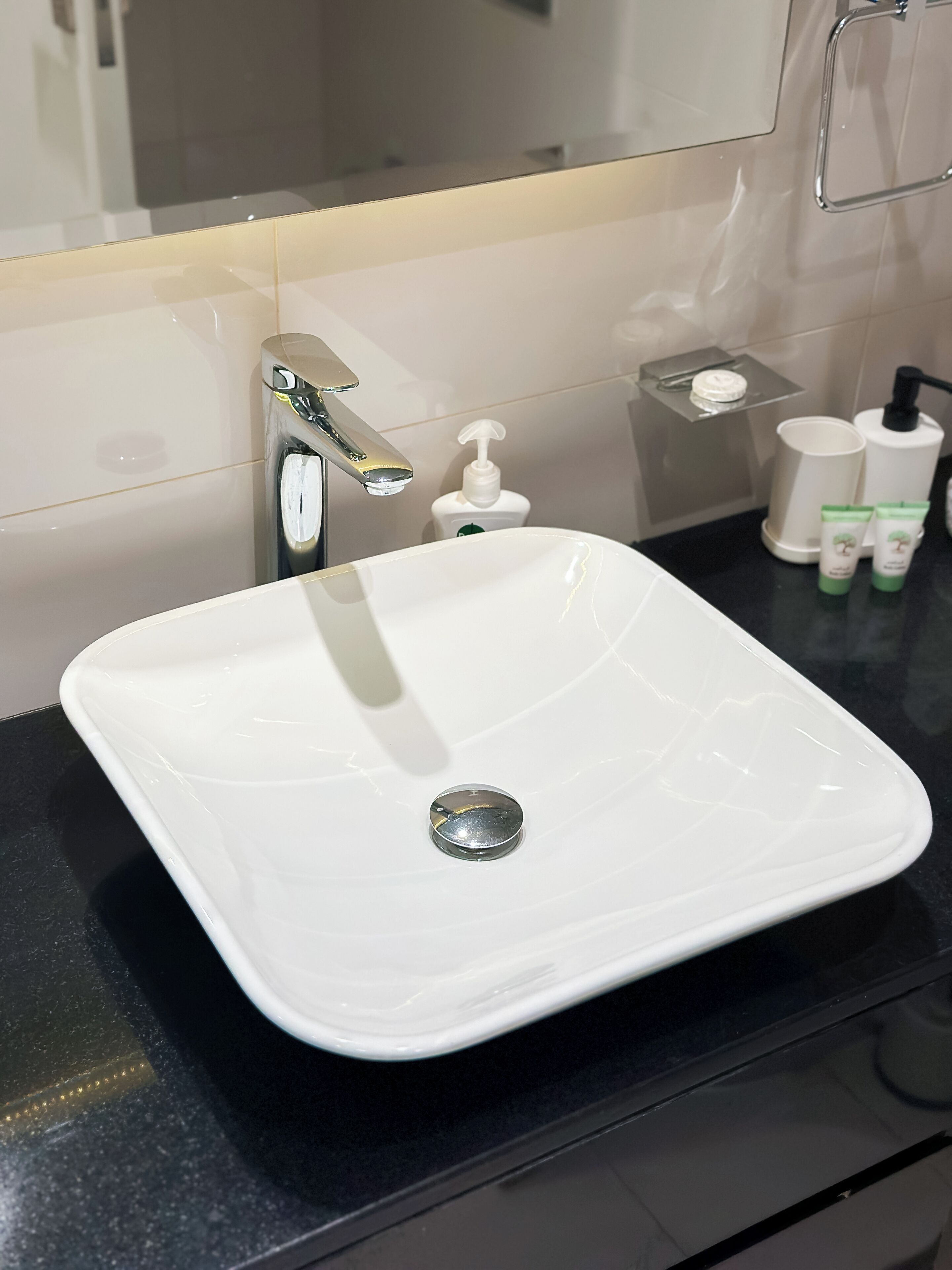 A white bathroom sink with a chrome faucet, a soap dispenser, and two toiletry bottles on a black countertop.
