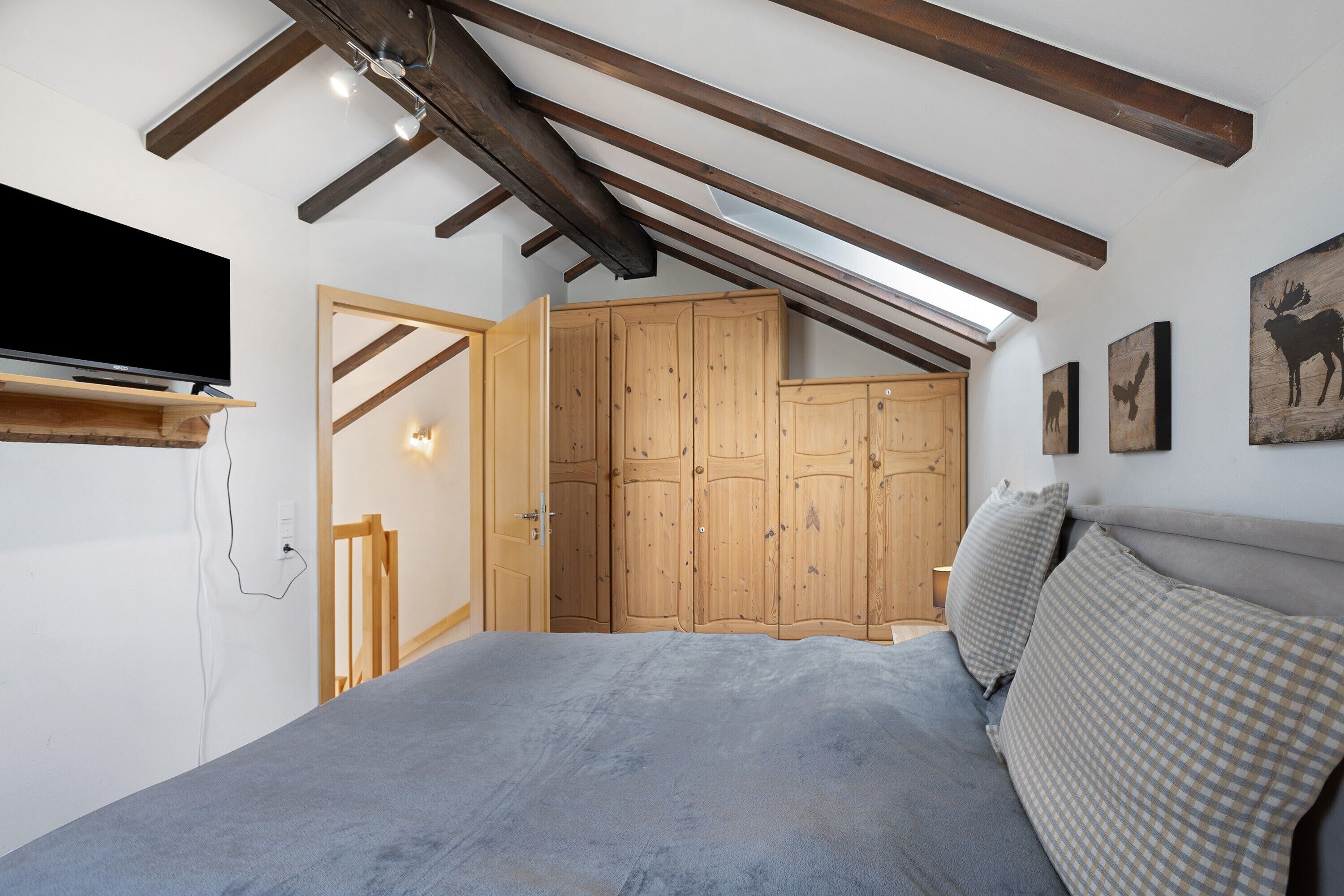 Une chambre à coucher avec un lit, une armoire en bois et un téléviseur fixé au mur.