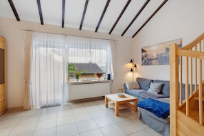 A living room with a sofa, a coffee table, a radiator, a window with curtains, a painting on the wall, and a staircase.