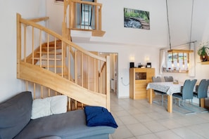 A modern interior with a wooden staircase, a dining area with a table and chairs, and a sofa with cushions.