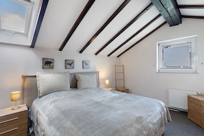 A bedroom with a large bed, wooden beams on the ceiling, a window, and wall-mounted artwork.