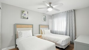 A hotel room with two single beds, a ceiling fan, and a window with patterned curtains. - Lighthouse Resort and Club (Sanibel)