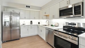 A modern kitchen with stainless steel appliances, white cabinetry, and a built-in microwave. - Lighthouse Resort and Club (Sanibel)