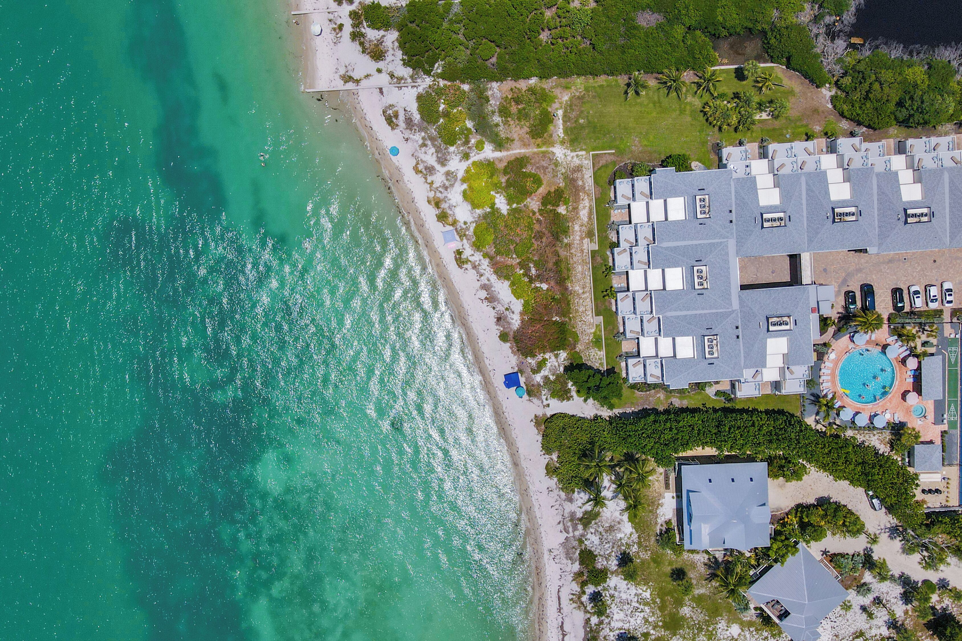 Vista aérea de uma propriedade costeira com piscina, vários edifícios e uma praia.