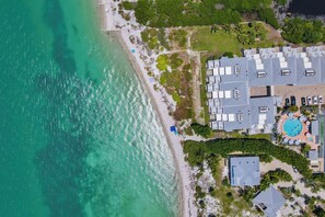 An aerial view of a coastal property with a swimming pool, multiple buildings, and a beach. - Lighthouse Resort and Club (Sanibel)