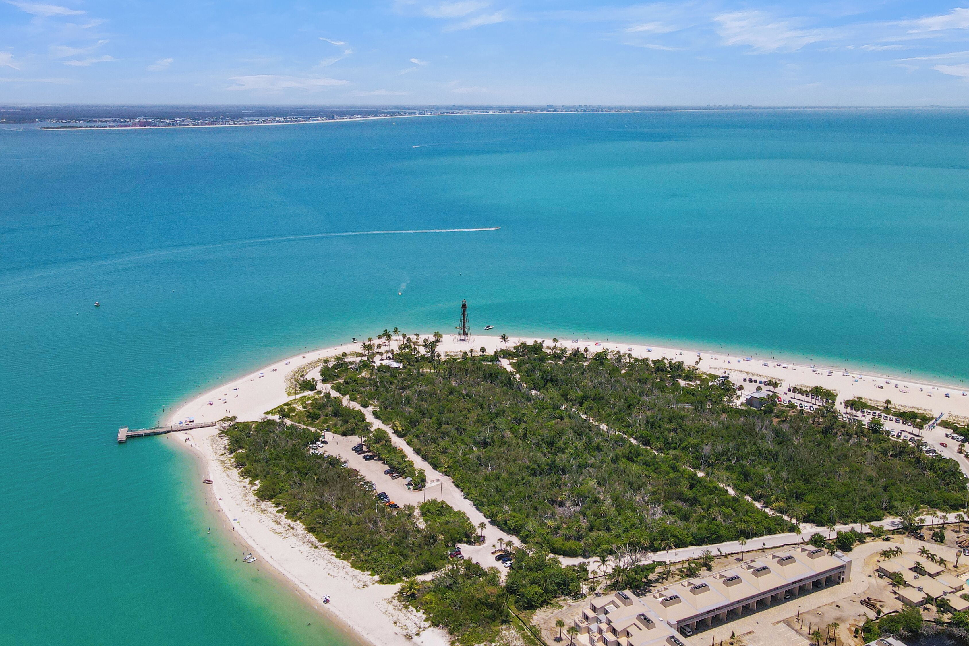 An aerial view of a coastal area with a beach, a pier, and a small island with dense vegetation.
