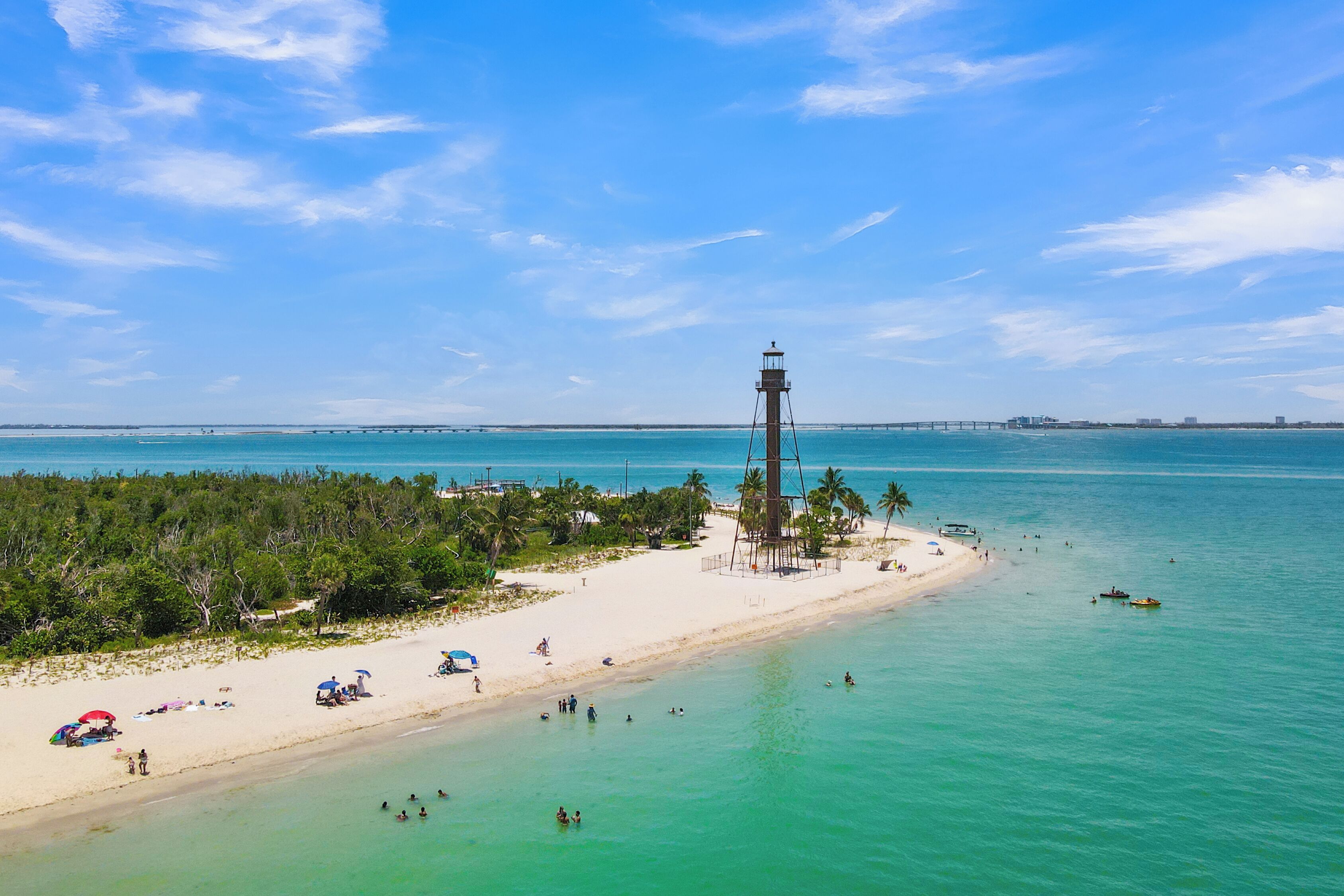 A beach with a lighthouse, clear turquoise waters, and a sandy shore.
