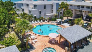 A resort with a central swimming pool surrounded by lounge chairs and umbrellas, with a view of the ocean and a bridge in the background. - Lighthouse Resort and Club (Sanibel)