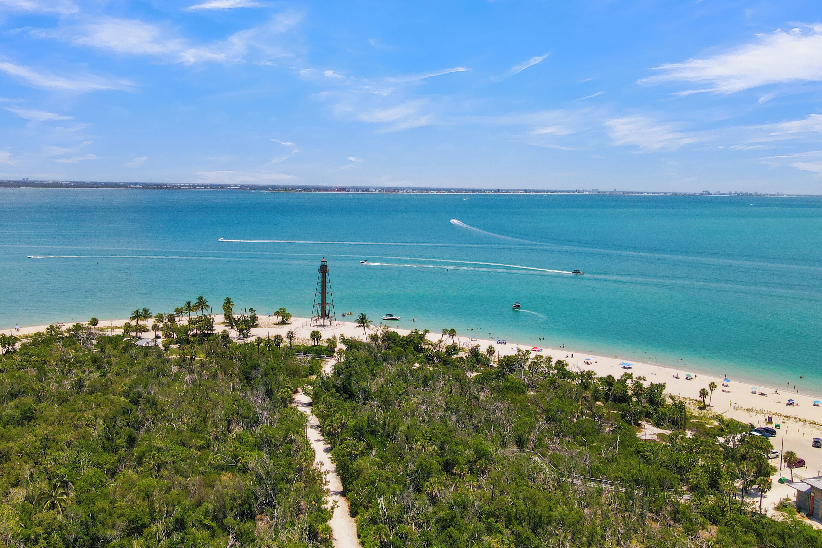 Ein Küstenstrand mit einem Leuchtturm, klarem blauen Wasser und einem Sandstrand.