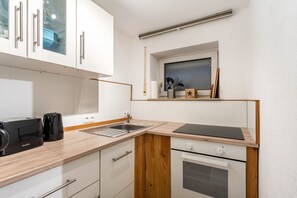 A compact kitchen with white cabinets, a built-in oven, a sink, and a small window above the countertop.