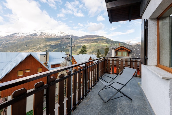 Un balcon avec vue sur les montagnes, une clôture en bois et une chaise.