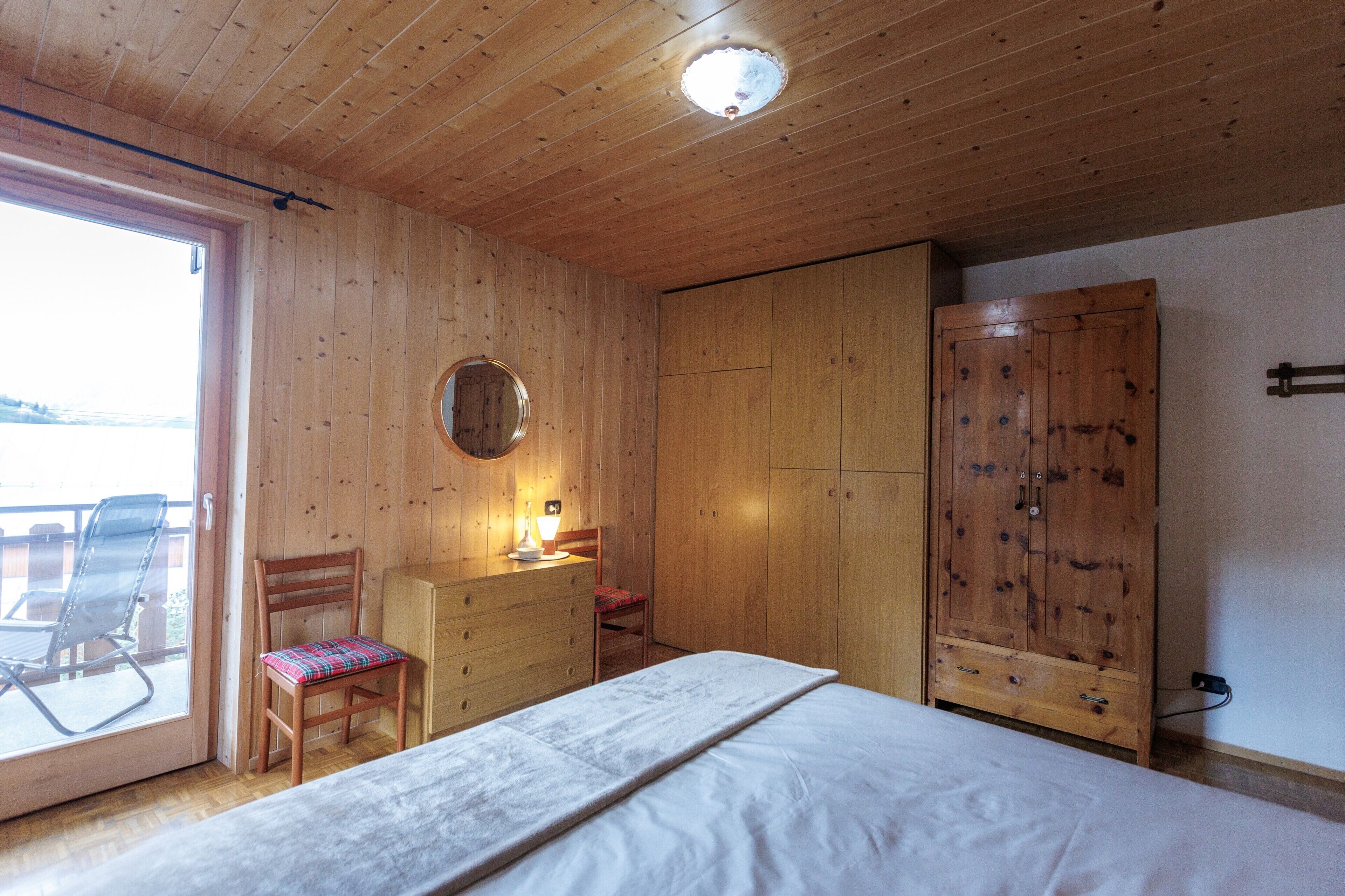 A wooden-paneled room with a bed, dresser, and a large wardrobe.