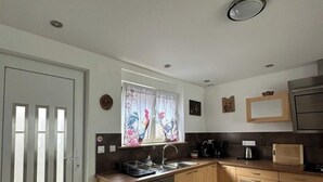 Eine kompakte Küche mit Holzausbau, integriertem Geschirrspüler, einem Fenster mit floralem Vorhang und einer kleinen Spüle.