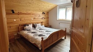 Ein Schlafzimmer mit Holzbalkendecke, einem hölzernen Bett mit gemustertem Überwurf und einem Fenster mit Blick ins Freie.