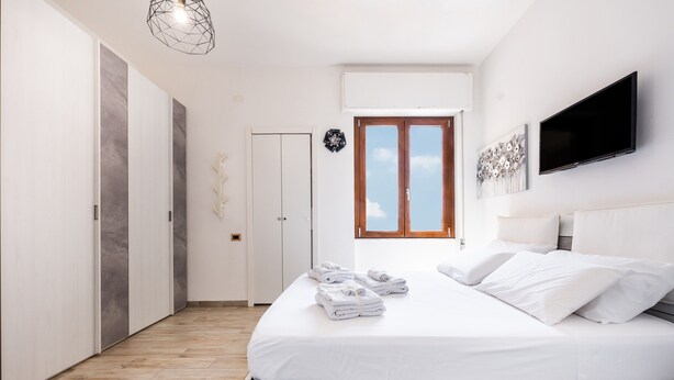 A bedroom with a bed, a TV, a window, and a door.