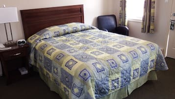 A hotel room with a bed, a chair, a nightstand with a phone, and a window with curtains.