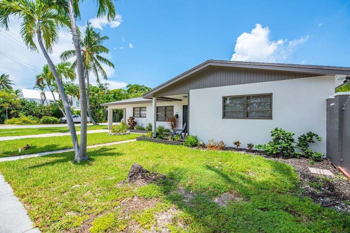 A modern two-story house with a white exterior, a covered porch, and a well-maintained lawn with palm trees.