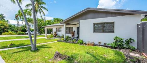 A modern two-story house with a white exterior, a covered porch, and a well-maintained lawn with palm trees.
