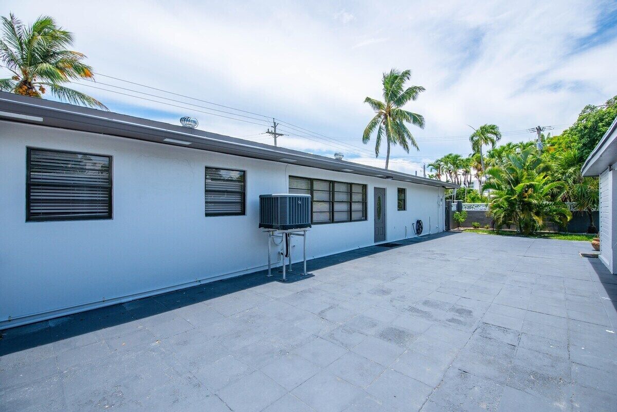 A modern building with a flat roof, large windows, and a covered outdoor area with a palm tree.