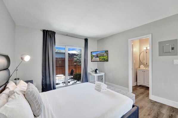 A bedroom with a bed, a bedside table, a TV, and a bathroom visible through an open door. - Pelican by Stay Hospitality (Pompano Beach)