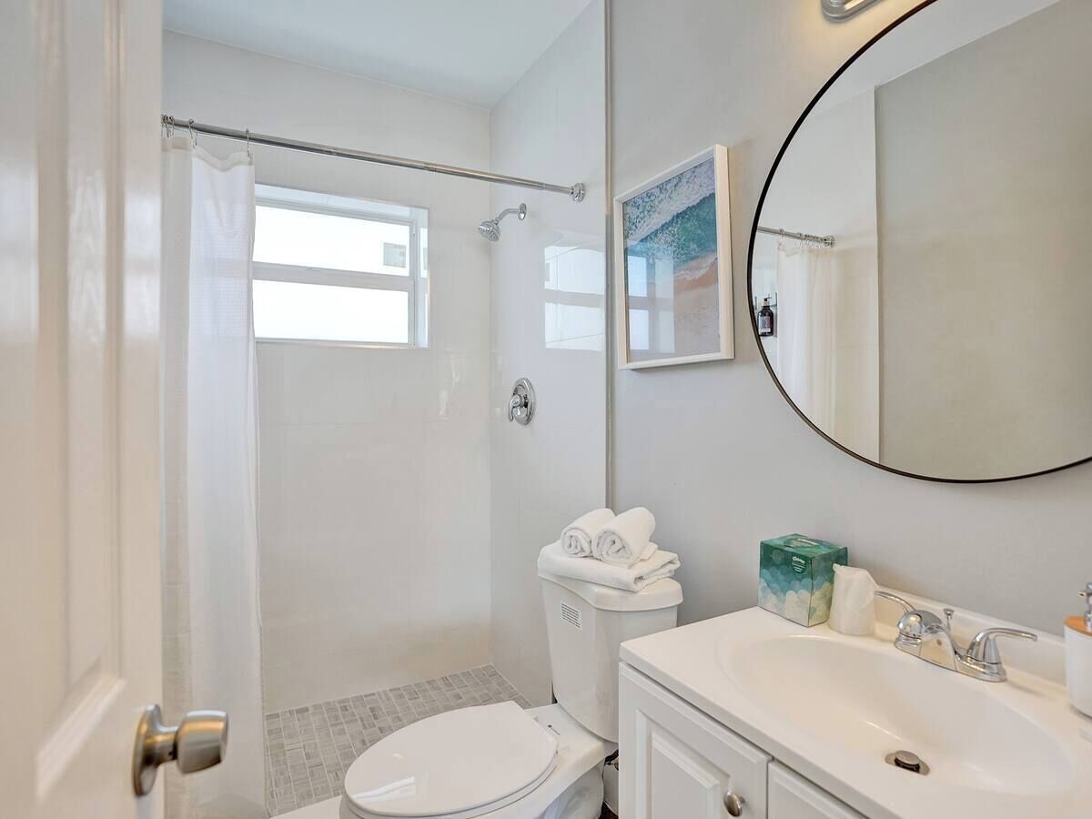 Un baño con inodoro, ducha, lavamanos y un espejo grande.
