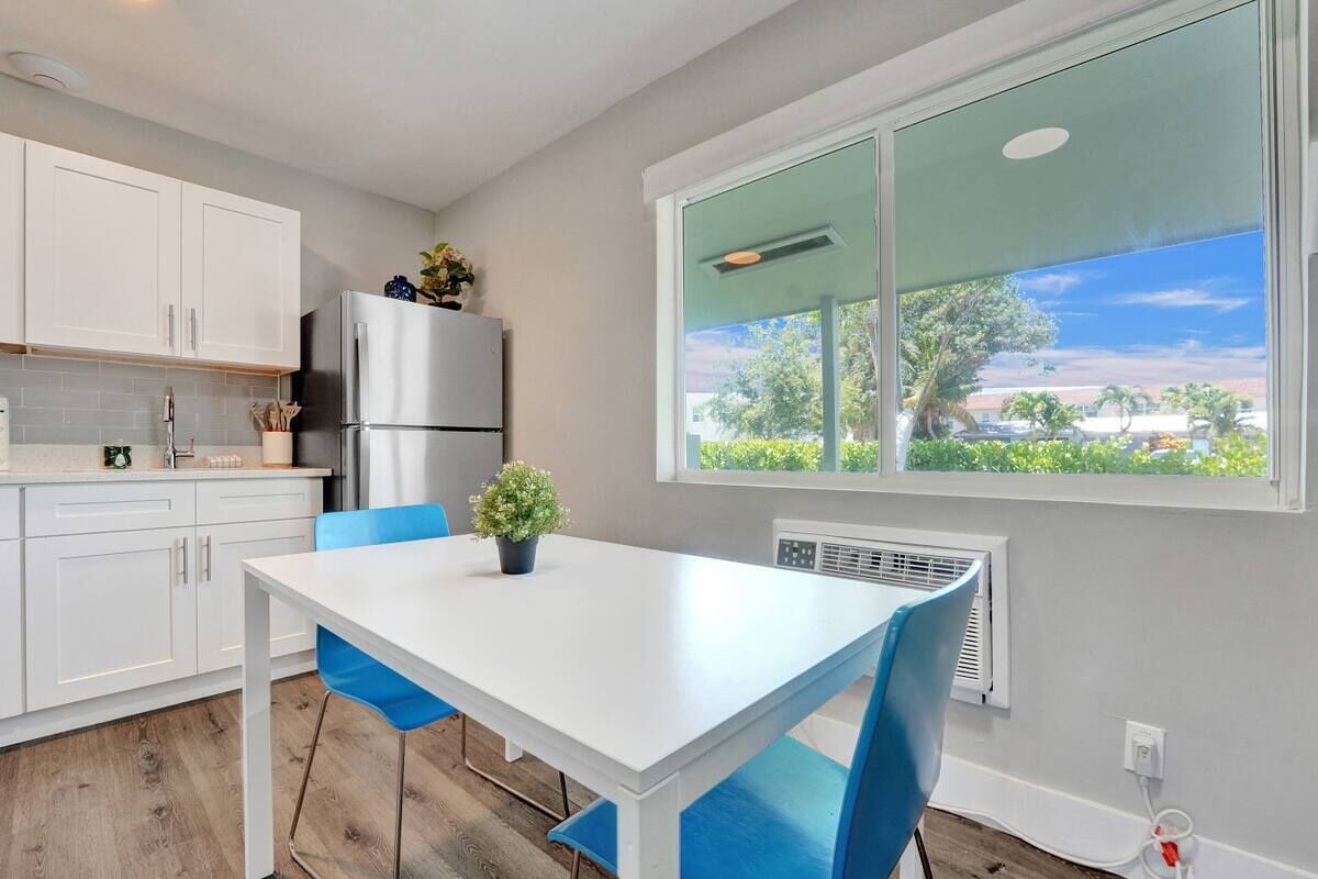 A kitchen with white cabinets, a stainless steel refrigerator, a white table, and blue chairs.
