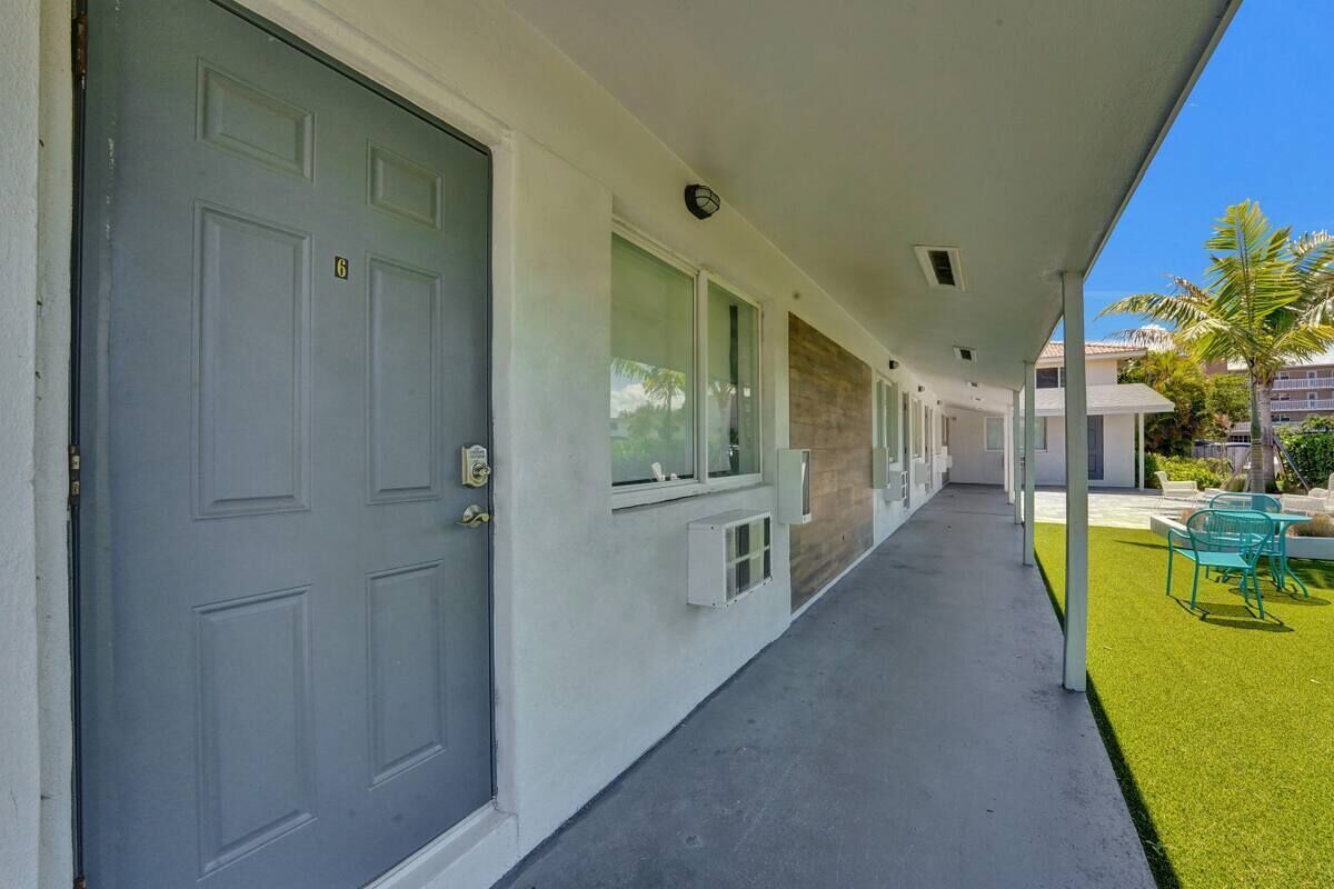 A covered walkway with a grey door, windows, and a small outdoor seating area with chairs.