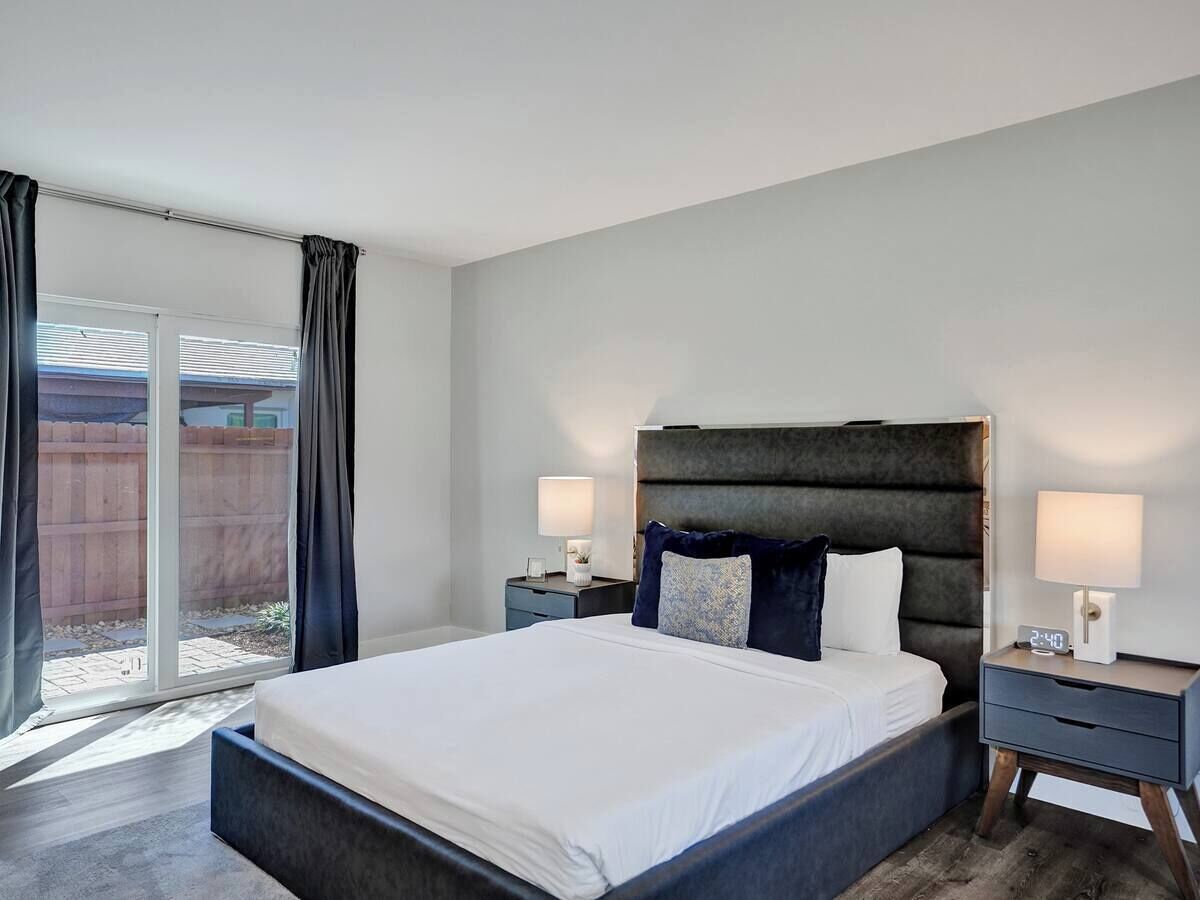 A modern bedroom with a large bed, two bedside tables with lamps, and a sliding glass door leading to an outdoor area.