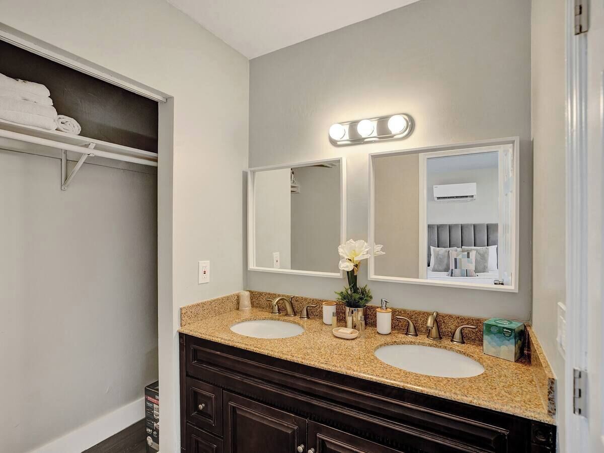 Une salle de bain avec deux lavabos, un meuble-lavabo avec des placards en bois foncé, un grand miroir avec éclairage intégré et un porte-serviettes avec des serviettes pliées.