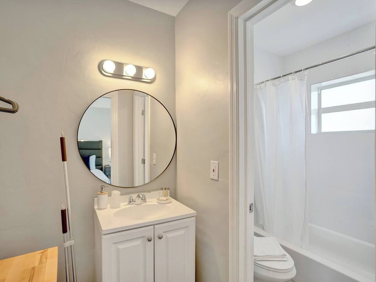 A bathroom with a white vanity, a round mirror, and a shower curtain.