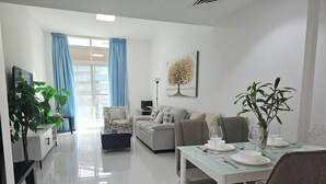 En moderne stue med sofa, spisebord og stole. Der er et fjernsyn på et stativ, en plante og et billede på væggen.