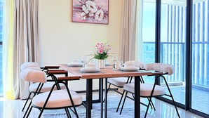 Un comedor con una mesa dispuesta para seis personas, una araña, un cuadro de flores y vistas de la ciudad a través de grandes ventanales.